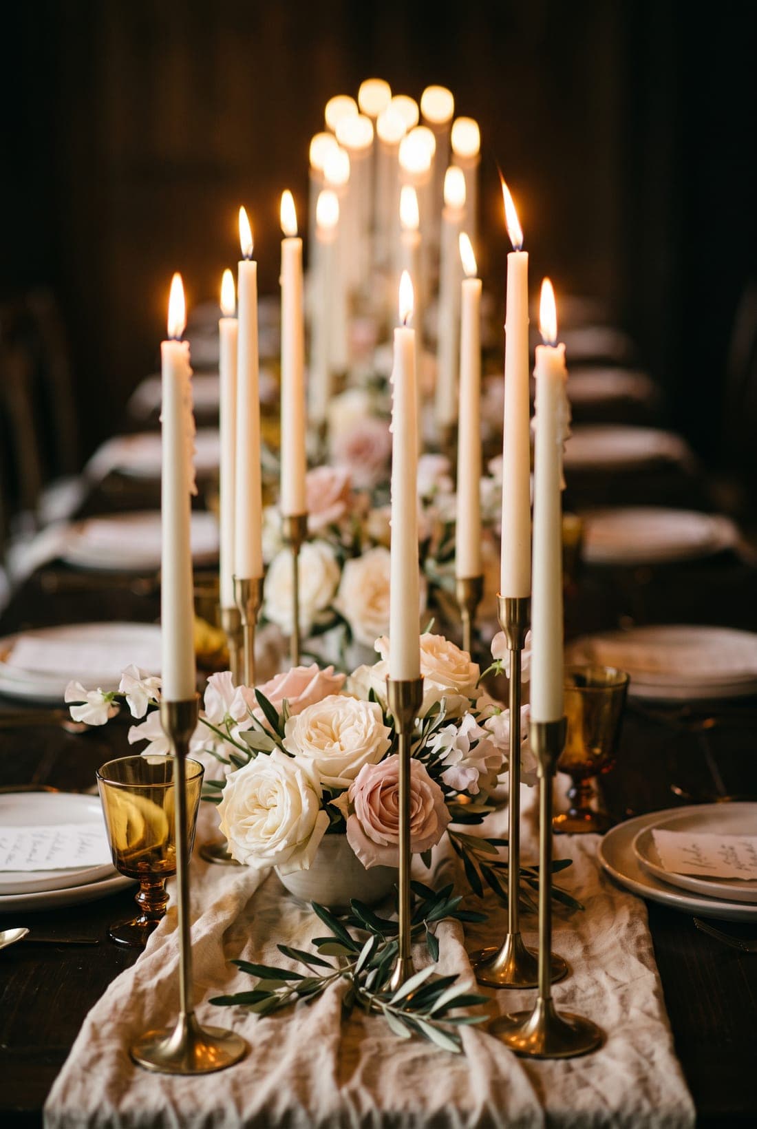Elfenbeinfarbene Stabkerzen und Gartenrosen auf einer kerzenerleuchteten Hochzeitstafel
